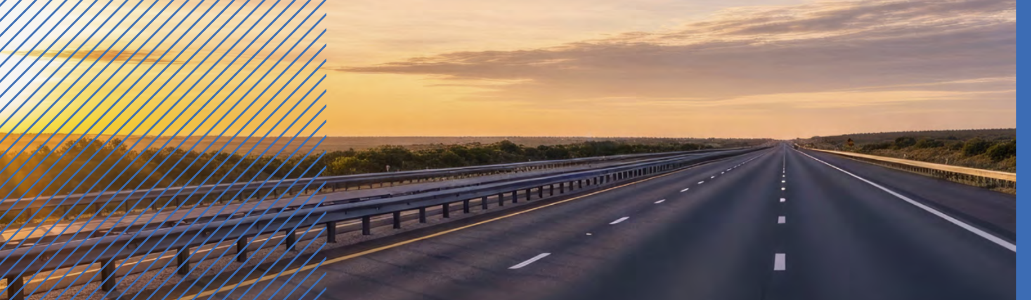 Empty highway with multiple lanes stretches into the distance under a cloudy sunset sky, bordered by low greenery; blue diagonal lines overlay the left side, reflecting themes from the National Road Safety Strategy.
