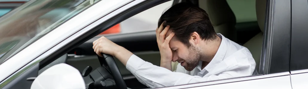 A car driver hesitating sits in the driver's seat, resting his head on his hand and appearing frustrated or stressed.